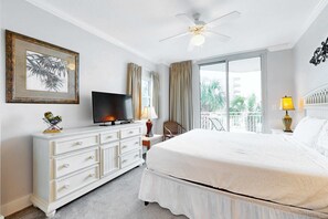 A hotel room with a bed, a TV, a dresser, a ceiling fan, a window with curtains, and a balcony view. - Second floor bright & Spacious condo with resort amenities, ocean views, & W&D (Fort Walton Beach)