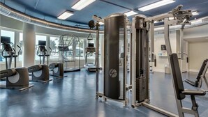 Uma academia com máquinas de cardio, equipamentos de musculação e amplas janelas.