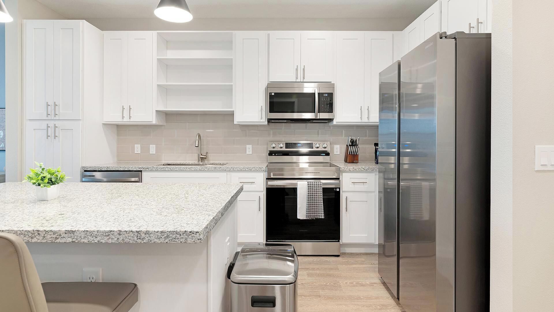 A modern kitchen with white cabinets, stainless steel appliances, a granite countertop, and a small island with a plant.