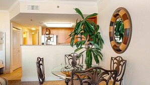 A dining area with a glass table, wooden chairs, a potted plant, and a decorative mirror on the wall. - 6th Floor Welcoming Condo At Waterscape Children's Playground, 2 Hot Tubs (Fort Walton Beach)