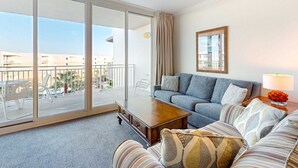 A modern living room with a sofa, a coffee table, and a view of the outside balcony. - 6th Floor Welcoming Condo At Waterscape Children's Playground, 2 Hot Tubs (Fort Walton Beach)