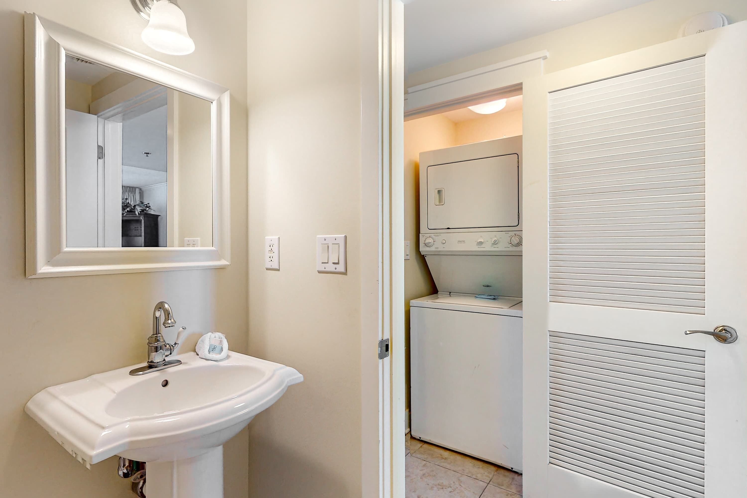 A bathroom with a white sink, mirror, and a door leading to a laundry area with a washing machine and dryer.