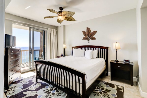 A hotel room with a bed, nightstands, a TV, and a balcony with a view of the ocean. - Gorgeous waterfront condo with incredible views, two pools & gym (Panama City Beach)
