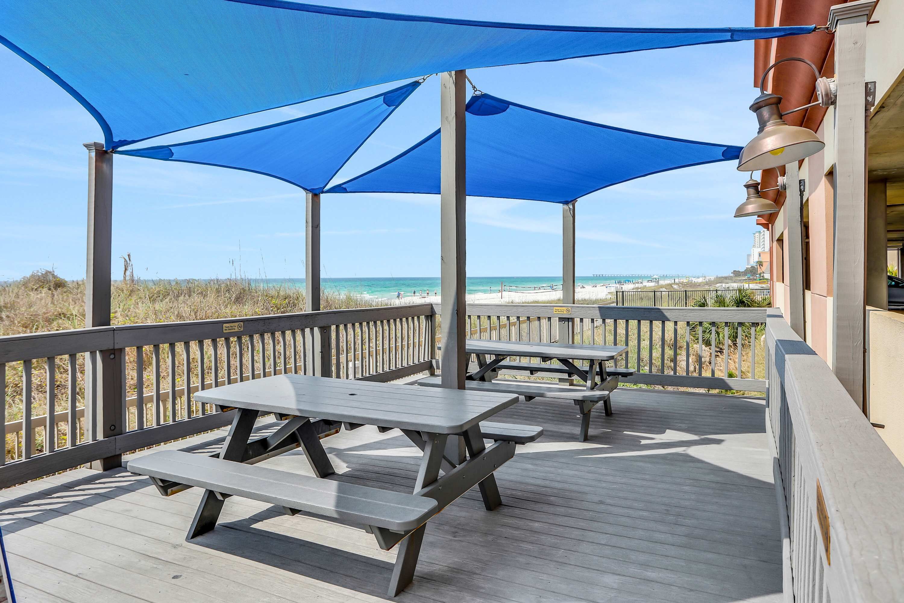 Une terrasse en bois avec des tables de pique-nique et un auvent bleu donnant sur la plage.