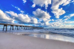 A beach with a wooden pier extending into the ocean under a partly cloudy sky. - Gorgeous waterfront condo with incredible views, two pools & gym (Panama City Beach)