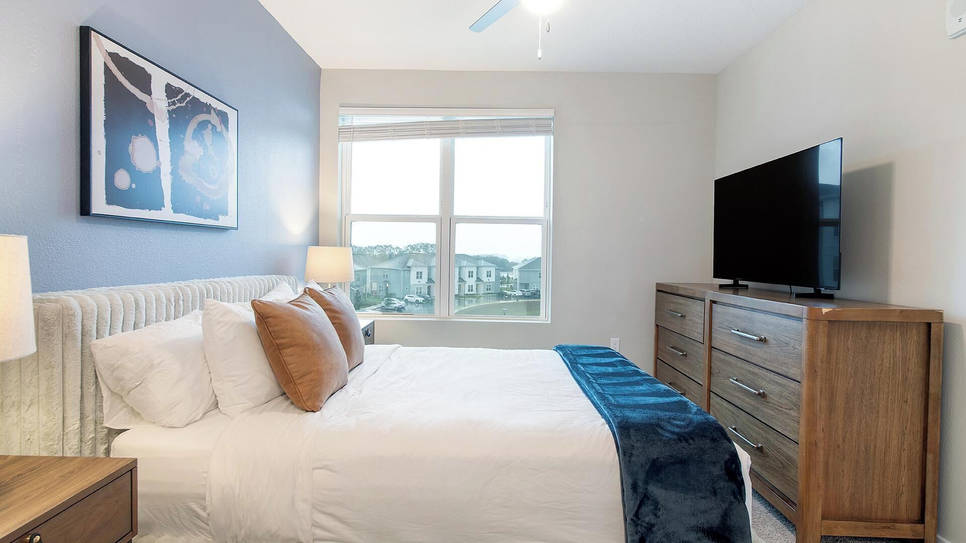 Une chambre d’hôtel avec un lit, une télévision, une commode et une fenêtre donnant sur des immeubles.