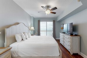 A bedroom with a large bed, a ceiling fan, a dresser, a TV, and a view of the outdoors. - Elegant, beachfront condo with two pools, BBQ area & fitness room (Panama City Beach)