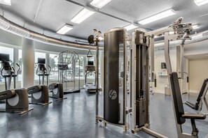 Ein Fitnessstudio mit verschiedenen Trainingsgeräten, darunter Laufbänder und Kraftmaschinen, in einem großzügigen Raum mit großen Fenstern, die für natürliches Licht sorgen.