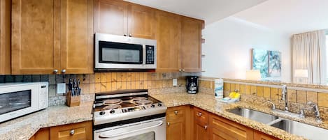A kitchen with wooden cabinets, a microwave, a stove, and a sink.
