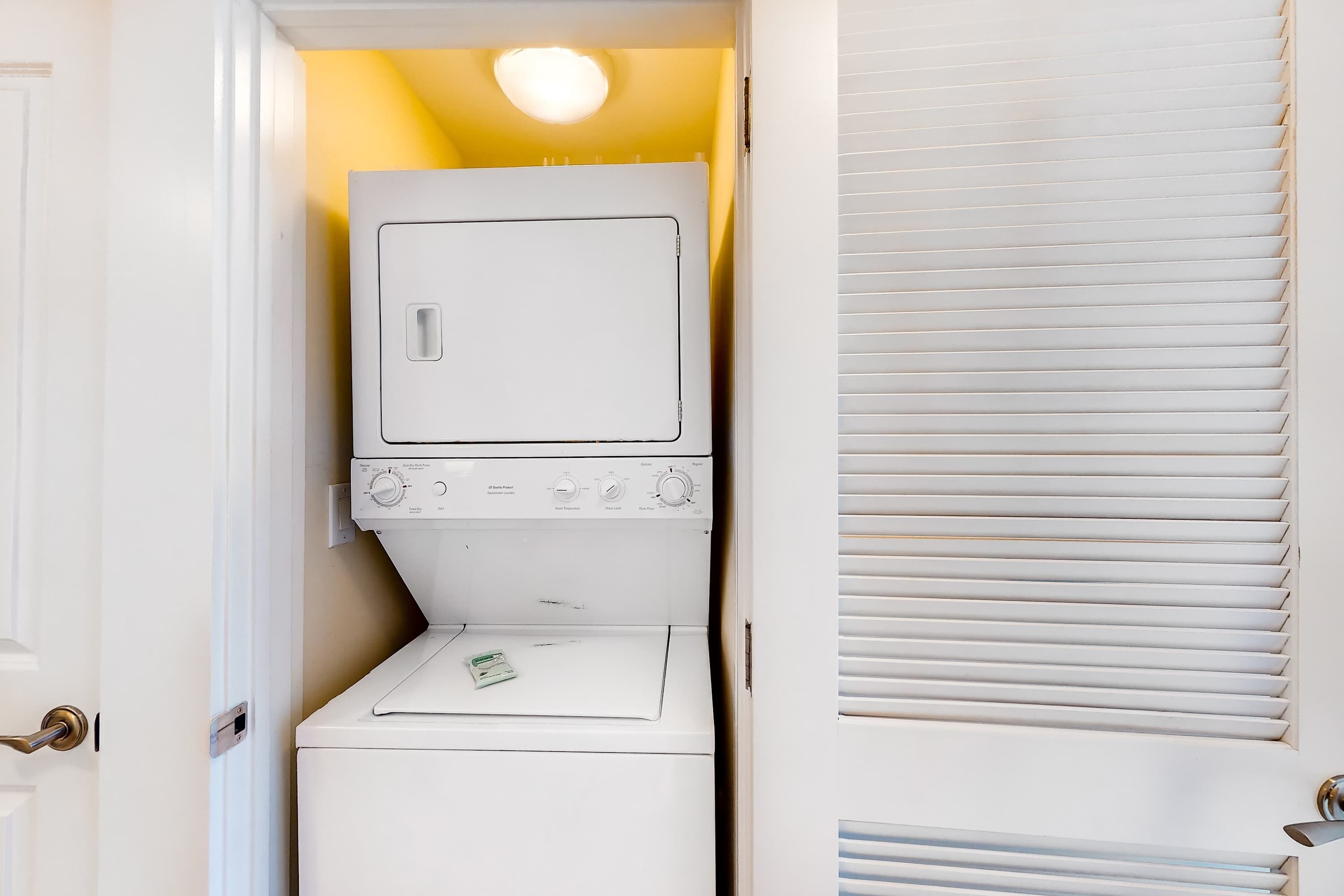 A compact laundry room with a washer and dryer, a small shelf, and a door with a handle.
