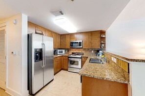 A modern kitchen with stainless steel appliances, wooden cabinets, and a granite countertop. - Condo On Okaloosa Island Children's Playground, 2 Hot Tubs (Fort Walton Beach)