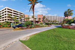 A multi-story hotel with a parking garage, palm trees, and well-maintained lawns. - 2nd-floor condo with balcony at Waterscape Waterfall, lazy river & beach chairs (Fort Walton Beach)