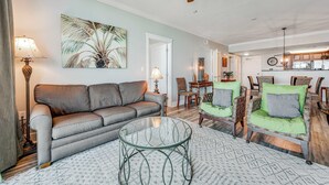 A living room with a sofa, chairs, a glass coffee table, and a ceiling fan. - Cozy, Tropical Condo On Okaloosa Island, Children's Playground, 2 Hot Tubs (Fort Walton Beach)