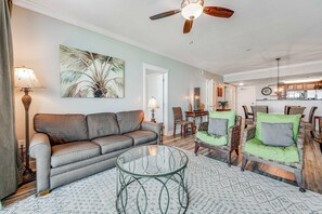 A living room with a sofa, chairs, a glass coffee table, and a ceiling fan. - Cozy, Tropical Condo On Okaloosa Island, Children's Playground, 2 Hot Tubs (Fort Walton Beach)