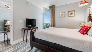 A hotel room with a large bed, a television, a desk with a lamp, and a window with curtains. - Cozy, Tropical Condo On Okaloosa Island, Children's Playground, 2 Hot Tubs (Fort Walton Beach)