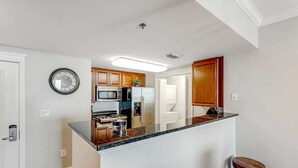 A modern kitchen with a central island, wooden cabinets, stainless steel appliances, and a clock on the wall. - Cozy, Tropical Condo On Okaloosa Island, Children's Playground, 2 Hot Tubs (Fort Walton Beach)
