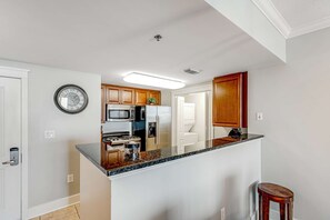 A modern kitchen with a central island, wooden cabinets, stainless steel appliances, and a clock on the wall. - Cozy, Tropical Condo On Okaloosa Island, Children's Playground, 2 Hot Tubs (Fort Walton Beach)
