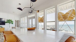 Una cucina moderna con una grande isola, piani di lavoro in marmo bianco e vista sull'oceano.