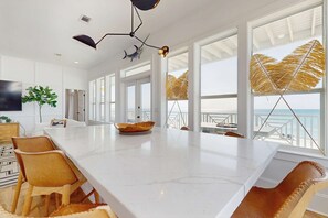 Une cuisine moderne dotée d’un grand îlot central, de plans de travail en marbre blanc et offrant une vue sur l’océan.