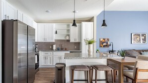 Una cocina moderna con electrodomésticos de acero inoxidable, armarios blancos y una isla central con taburetes de bar.