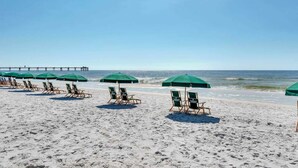 A beach with rows of green umbrellas and wooden lounge chairs. - Inviting, Spacious Condo On Okaloosa Island Waterfall, Lazy River (Fort Walton Beach)