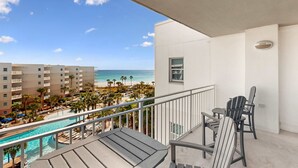 Ein Balkon mit Blick auf Pool und Strand, ausgestattet mit Tisch und Stühlen.