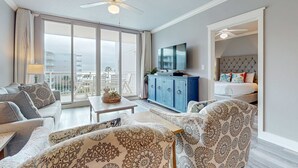 Une chambre d’hôtel moderne dotée d’un balcon, d’un ventilateur de plafond, d’une télévision, d’un lit avec une tête de lit capitonnée et de meubles à motifs.