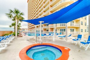 A pool area with lounge chairs, a hot tub, and a building with balconies. - Gulf-front condo with balcony, beach views, pool, hot tub & gym (Panama City Beach)