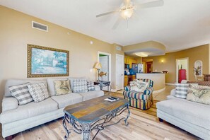 A living room with a sofa, armchair, coffee table, and a painting on the wall. - Gulf-front condo with balcony, beach views, pool, hot tub & gym (Panama City Beach)
