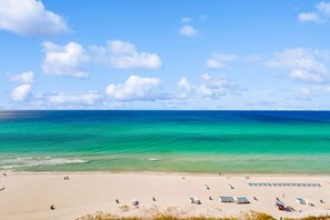 A beach with clear turquoise waters, a sandy shore, and several beach umbrellas and sun loungers. - Gulf-front condo with balcony, beach views, pool, hot tub & gym (Panama City Beach)