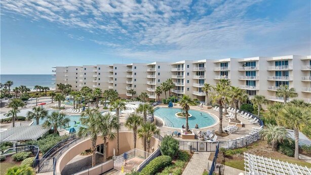 Un hôtel à étages, avec une piscine entourée de palmiers et offrant une vue sur l’océan.