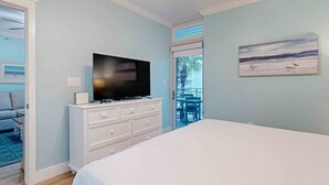 Une chambre à coucher avec un lit, un téléviseur posé sur une commode, un tableau accroché au mur et une vue sur l’extérieur.