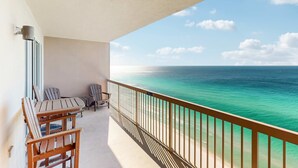 A balcony with a view of the ocean, wooden chairs, and a table. - Gulf-view condo with beach service, pools, hot tubs & gym (Panama City Beach)