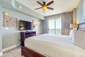 Ein Hotelzimmer mit einem großen Bett, einem Deckenventilator, einem Flachbildfernseher, einem Wandbild und Blick auf den Außenbalkon.