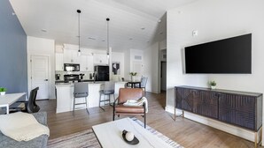 Ein moderner Wohnraum mit Küche, Essbereich und einem an der Wand befestigten Fernseher.