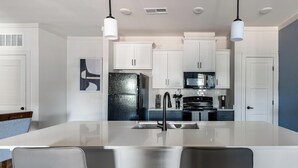 Una cocina moderna con armarios blancos, un refrigerador negro, un lavamanos de acero inoxidable y una isla central con sillas.