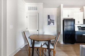 Une cuisine compacte avec des meubles blancs, un réfrigérateur noir et un coin repas comprenant une table ronde et deux chaises.