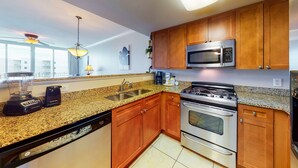 A modern kitchen with granite countertops, stainless steel appliances, wooden cabinets, and a ceiling fan. - Warm, Welcoming Condo On Okaloosa Island 490 Feet Of Private Beach (Fort Walton Beach)