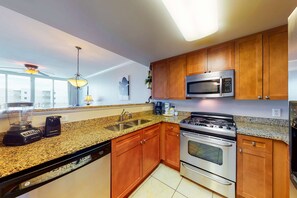 Eine moderne Küche mit Granit Arbeitsplatten, Edelstahlgeräten, Holzschränken und einem Deckenventilator.