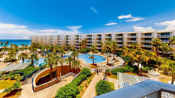 A resort with a central pool, palm trees, and a view of the ocean. - Warm, Welcoming Condo On Okaloosa Island 490 Feet Of Private Beach (Fort Walton Beach)