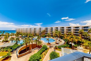 A resort with a central pool, palm trees, and a view of the ocean. - Warm, Welcoming Condo On Okaloosa Island 490 Feet Of Private Beach (Fort Walton Beach)