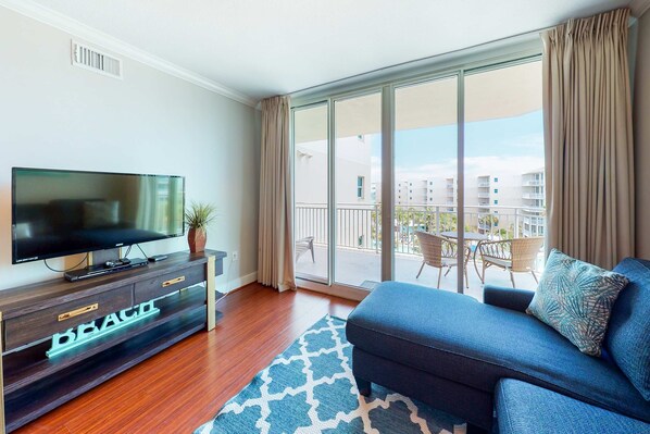 A modern living room with a flat-screen TV, a dark blue sofa, and a patterned rug. - Warm, Welcoming Condo On Okaloosa Island 490 Feet Of Private Beach (Fort Walton Beach)