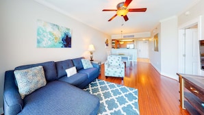 A living room with a sofa, patterned rug, ceiling fan, and a view into the kitchen. - Warm, Welcoming Condo On Okaloosa Island 490 Feet Of Private Beach (Fort Walton Beach)