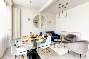 Ein modernes Wohnzimmer mit einem Glastisch, weißen Stühlen, einem blauen Sofa und einem grauen Sessel.