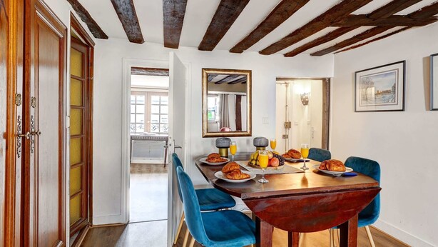 A dining area with a wooden table, blue chairs, and breakfast items. - Ile Saint-Louis 2BR - Notre-Dame & Sainte-Chapelle (Paris)