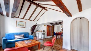 A spacious living area with a blue sofa, red chairs, and a wooden coffee table. A kitchen is visible in the background with a dining area. - Ile Saint-Louis 2BR - Notre-Dame & Sainte-Chapelle (Paris)