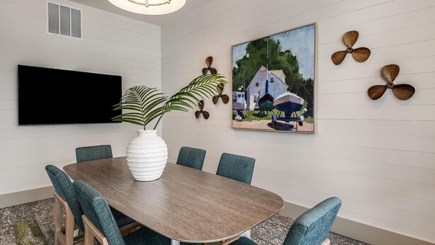 Una sala de conferències amb una taula rodona, sis cadires, un televisor de pantalla plana, un quadre i elements decoratius a la paret.