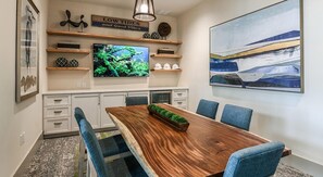 A dining area with a wooden table, blue chairs, a television, and decorative items on shelves. - Landing | Stunning 1BD, Clubhouse, Gym (Apopka)