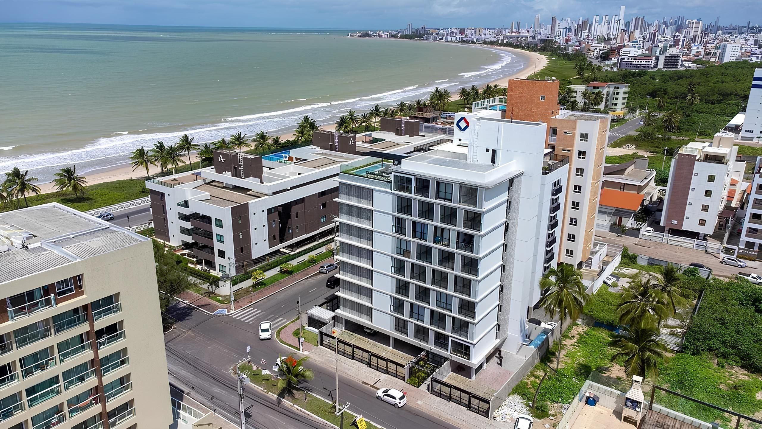 A modern building with multiple floors, a rooftop pool, and a view of the beach and ocean.