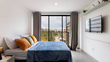 A modern bedroom with a bed, a TV, and a city view.